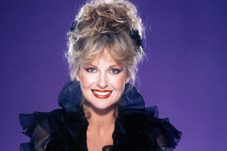 Shelley Fabares smiles for a portrait against a purple background