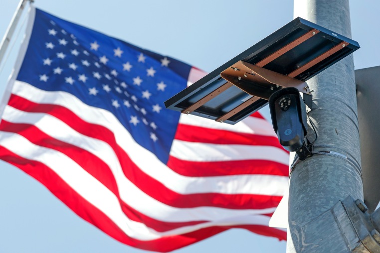 An American flag flies behind a Flock Safety camera tmounted to a light pole