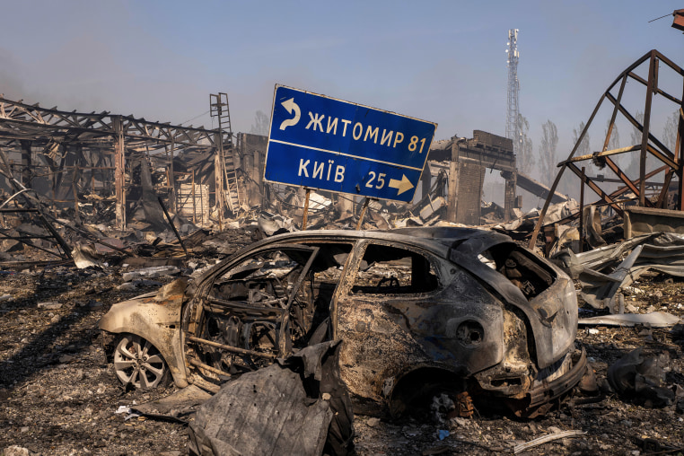 A burned car sitting in the midst of further wreckage after an explosion.