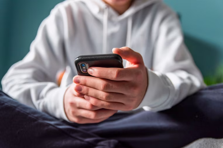 Close up of hands of teen boy in white sweater texting on phone.