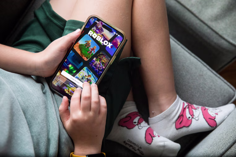 A child holds a smartphone displaying the Roblox app login page