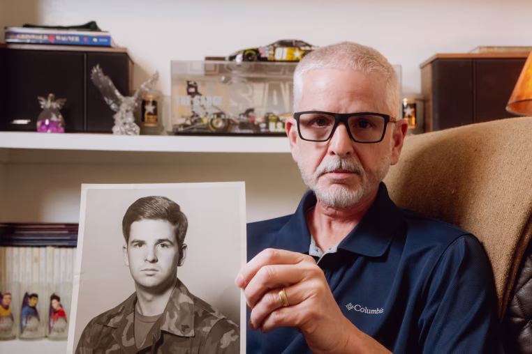 FORT WORTH, TEXAS - FEBRUARY 11, 2026: Guy Shoemaker, 64, displays his AIT platoon sergeant leadership photograph from his time as an Army recruiting officer at his home in Fort Worth, Texas, on Wednesday, Feb. 11, 2026. After his TRICARE plan transitioned to TriWest Healthcare Alliance, tens of thousands of dollars in previously approved claims for life-saving treatment and scans for his throat cancer were pulled back or denied because of a data error.