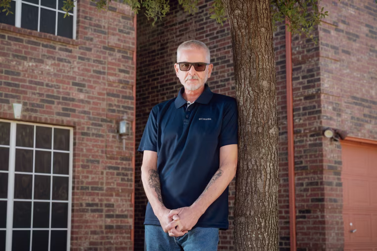FORT WORTH, TEXAS - FEBRUARY 11, 2026: Guy Shoemaker, 64, poses for a portrait outside his home in Fort Worth, Texas, on Wednesday, Feb. 11, 2026. After his TRICARE plan transitioned to TriWest Healthcare Alliance, tens of thousands of dollars in previously approved claims for life-saving treatment and scans for his throat cancer were pulled back or denied because of a data error.