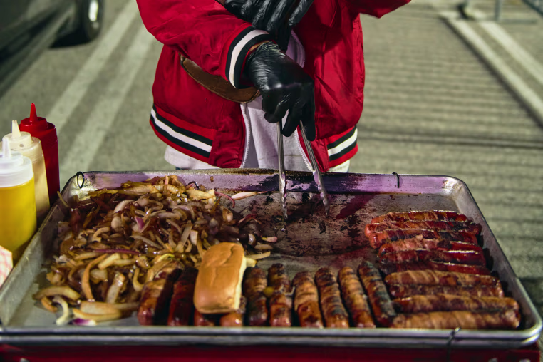 Henrry Josue uses tongs to grab hotdogs on a tray outside