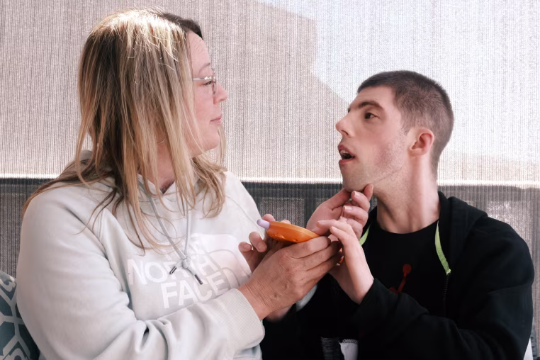 Melissa Gonce sits on a bench on a porch next to Jason, she has her hand on his chin as he holds an orange toy
