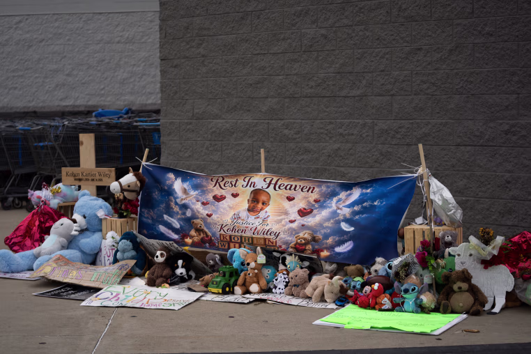 A memorial with balloons and stuffed animals in front of a Walmart.