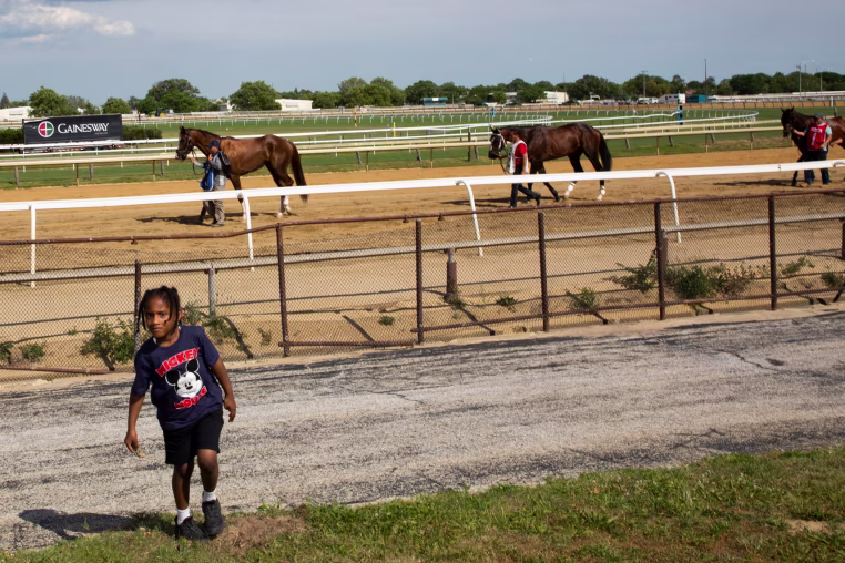 A young boy walks near a racetrack with racing horses.