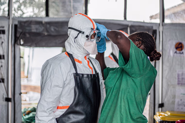 A hygiene worker helps a doctor put on personal protective equipment inside of a room