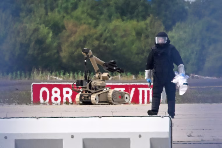 A forensic technician works alongside a bomb-disposal robot.