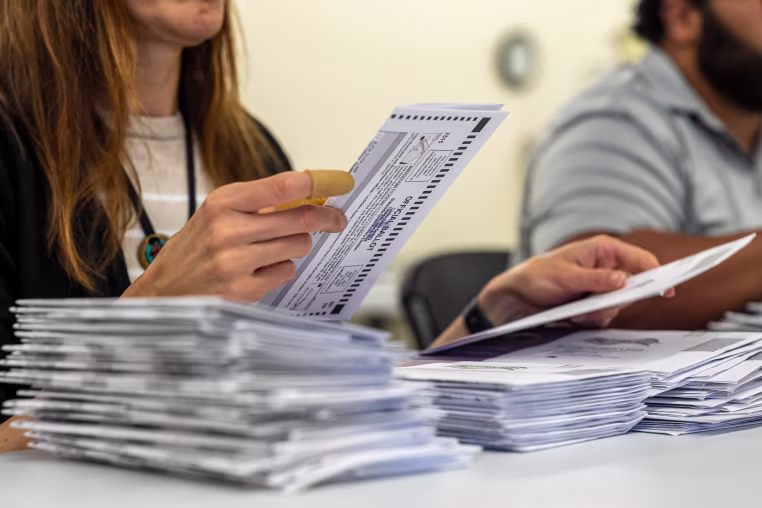 A woman extracts a mail-in ballot from an envelope. 