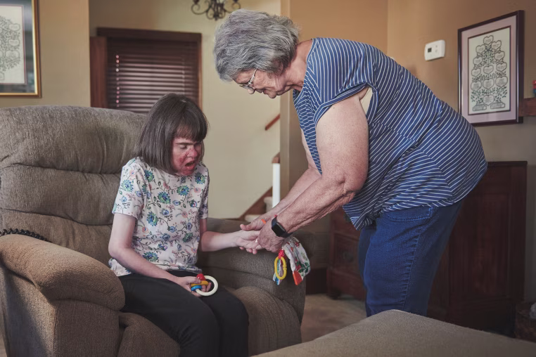 Image: Nancy Enstrom holding her daughter Anna's hand while assisting her at home.