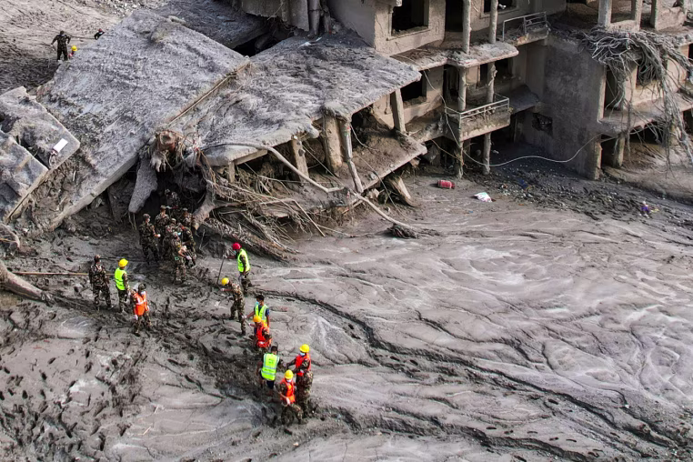 A drone view shows rescue workers inspect the area and damaged structures.