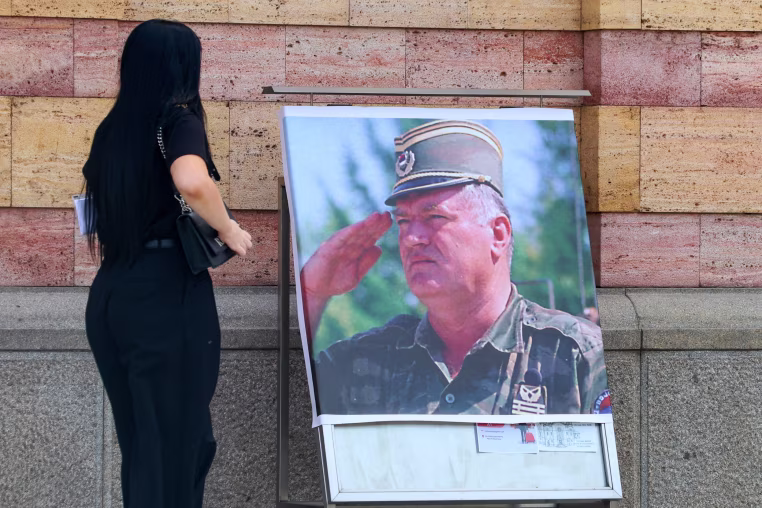 A woman watches a poster depicting former Bosnian Serb military chief Ratko Mladic displayed outside the Orthodox Cathedral