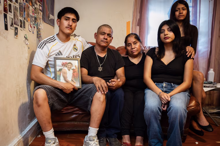 A grief-stricken family seated on a couch inside their living room.