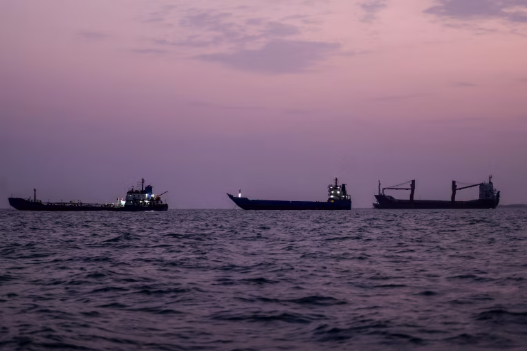 Three commercial vessels floating in the water at sunset.
