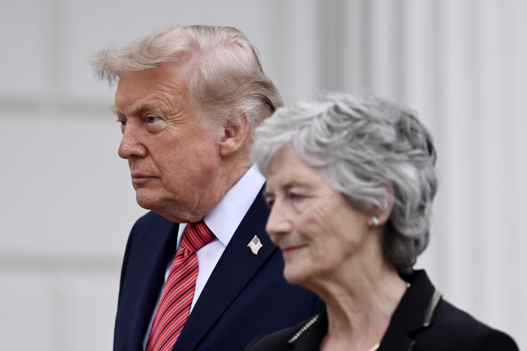 Donald Trump appears behind the Irish President Catherine Connolly as they walk outdoors.