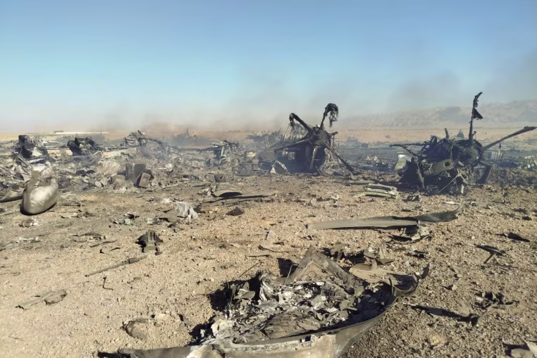 Charred remains of a fighter jet strewn over sandy ground.