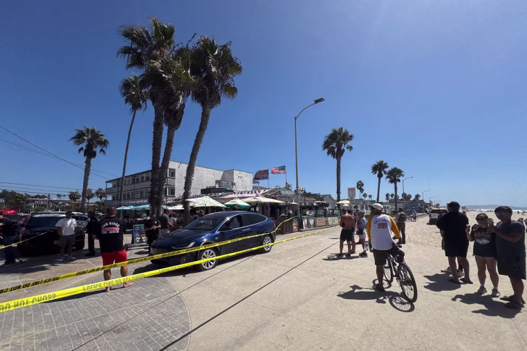 Bystanders look onto the scene in Pacific Beach after a blue Tesla.