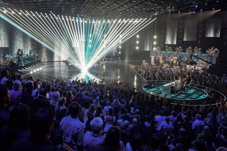 A wide view of the audience, judges, and a performer on stage during American Idol.