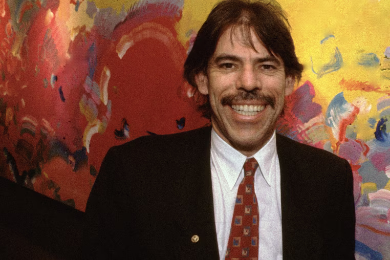 Peter Max smiles while standing in front of an oil painting.