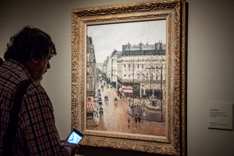 Museum goer looks at the painting 'Rue Saint-Honore por la tarde. Efecto de lluvia.'
