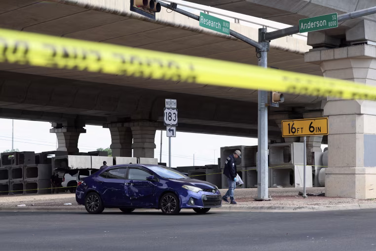 A dark blue Toyota car appears to have bullet holes while parked at an intersection behind yellow tape.