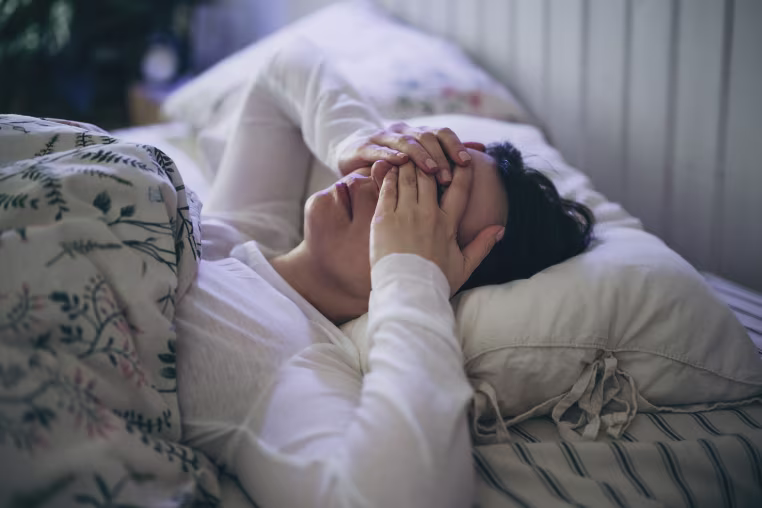 Sleepless young woman suffering from insomnia, covering eyes with hands