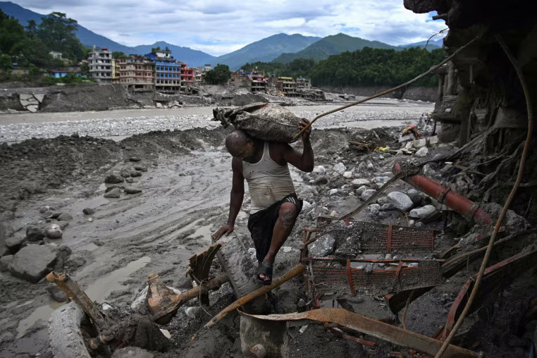 A man carrying a bag as he walks past a damaged house.