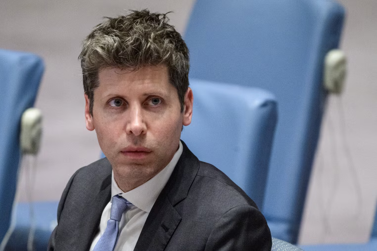 Sam Altman seated in a row of light blue upholstered chairs.