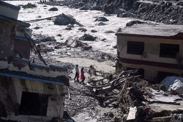 People walk past damaged houses.