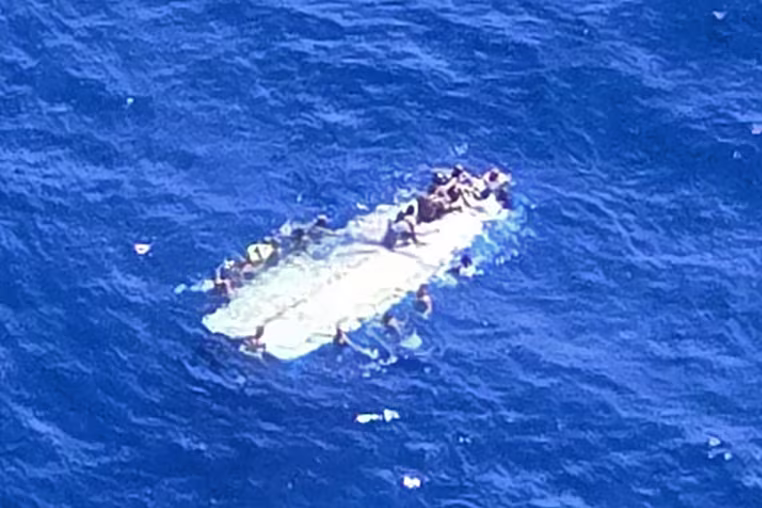 Image: Survivors hold on to a capsized makeshift vessel in the sea.