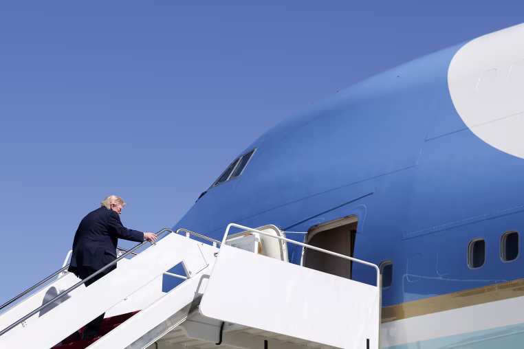 President Trump boarding Air Force one against a clear blue sky.
