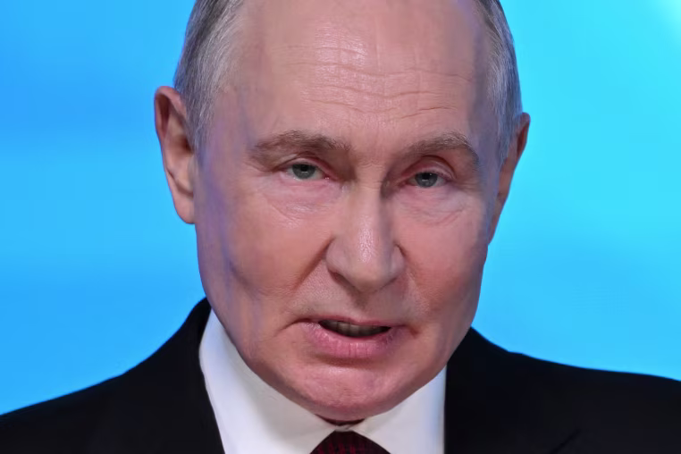 Vladimir Putin seen in a close view against an illuminated blue background.