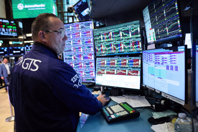 A trader looks at multiple computer screens at a desk