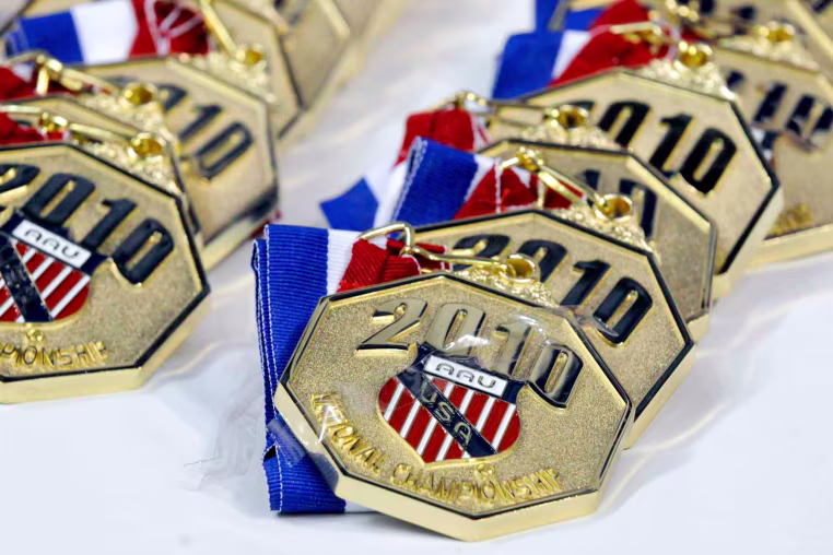 Gold medals with engraved text reading "2010 AAU USA National Championship" with an AAU crest in the center, lined up on a table