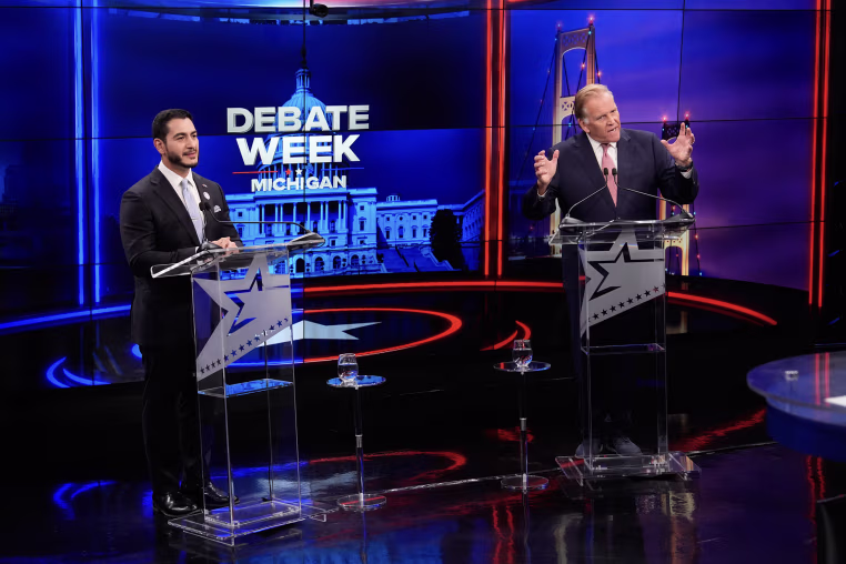 Abdul El-Sayed and Mike Rogers standing at matching lecterns during a debate.