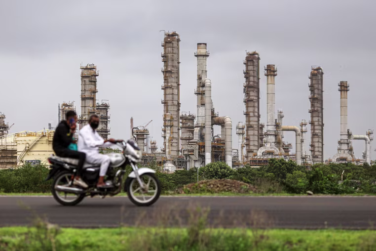 Image: Two men on a motorbike ride past an oil refinery in Jamnagar.
