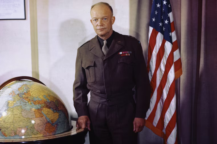 Portrait of Dwight Eisenhower standing between a large globe and an American flag
