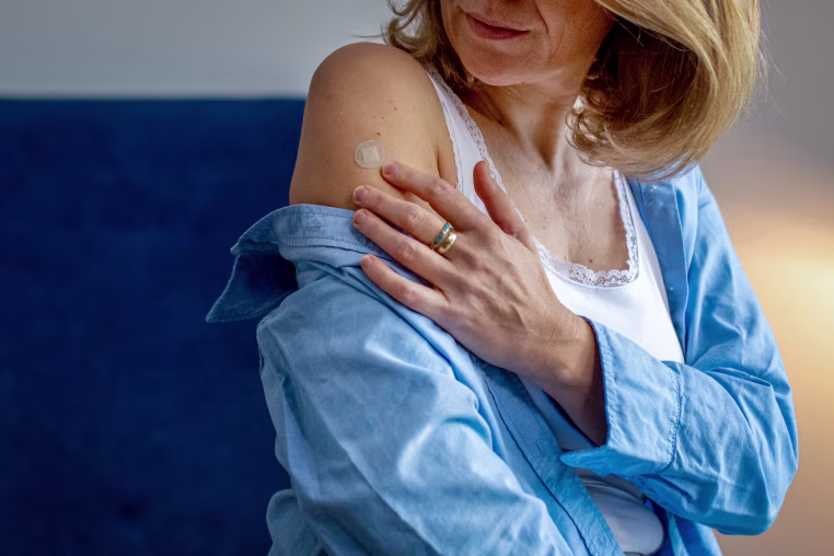 Woman applying estrogen patch during hormone therapy. Rear view.