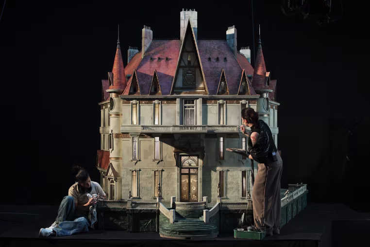 Two women put the final touches on a scale replica of a castle in a darkened room.