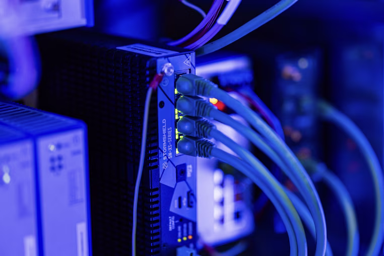 Networking cables plugged into glowing ports on the back of computing hardware. 