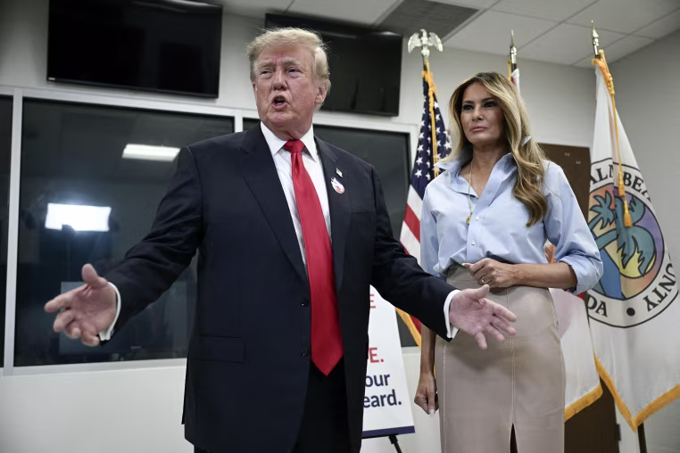 Donald and Melania Trump standing in front of a Florida state flag.