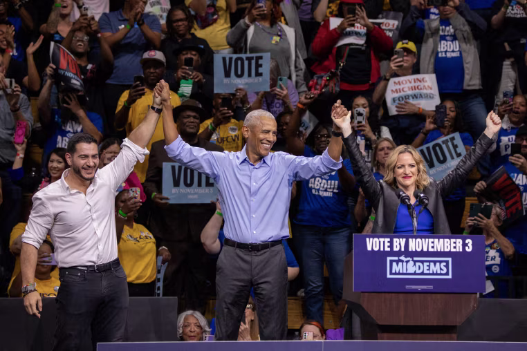 Barack Obama, Abdul El-Sayed and Jocelyn Benson join hands on stage during a rally.