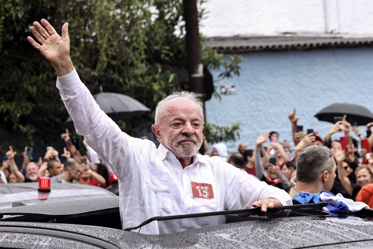 Luiz Inácio Lula Da Silva waves while standing up through a car's sun roof.
