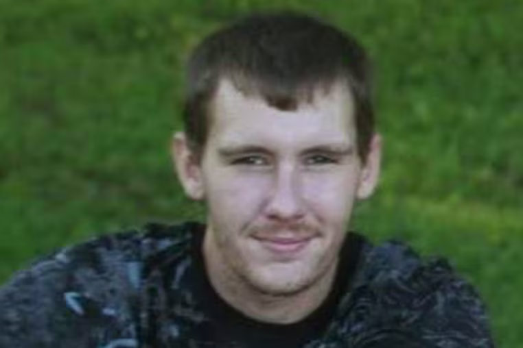 Cody Birchfield sits on a blanket on grass outside