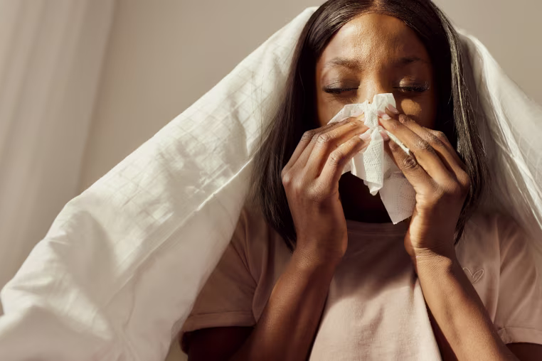 Sick black woman blowing her nose during morning in bedroom.