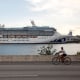 Image: A man rides a bicycle in front of the Coral Princess ship, of Princess Cruises fleet, docked at Miami Port with patients affected by coronavirus disease (COVID-19), in Miami