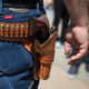 Image: A close-up of man's waist wearing an ammunition belt with bullets and a gun in a holster.