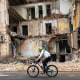Image: A cyclist passes by a building partially destroyed by a missile strike.