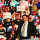 Image: Ron DeSantis speaks to a crowd during a campaign rally. A sign in the audience reads,\"Latinos for Trump\".